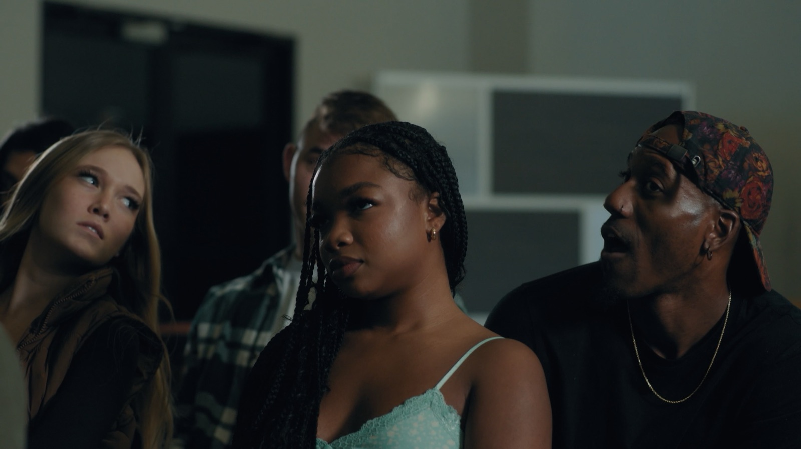 Cherie, braids over one shoulder, stares ahead in a crowd while a man beside her turns to speak. Still from My Cherie Amour.