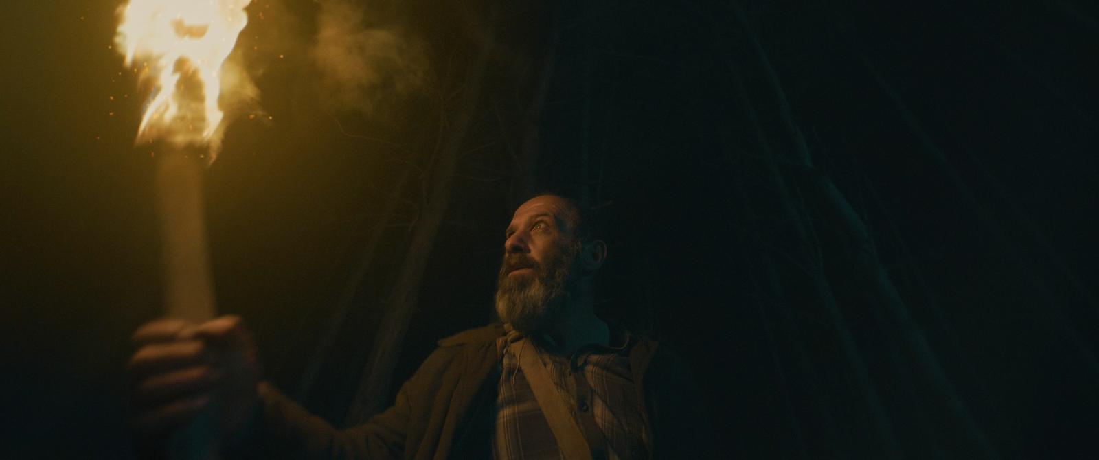Damien holds a torch in the dark. Still from OBITUS, courtesy of Recfilms.