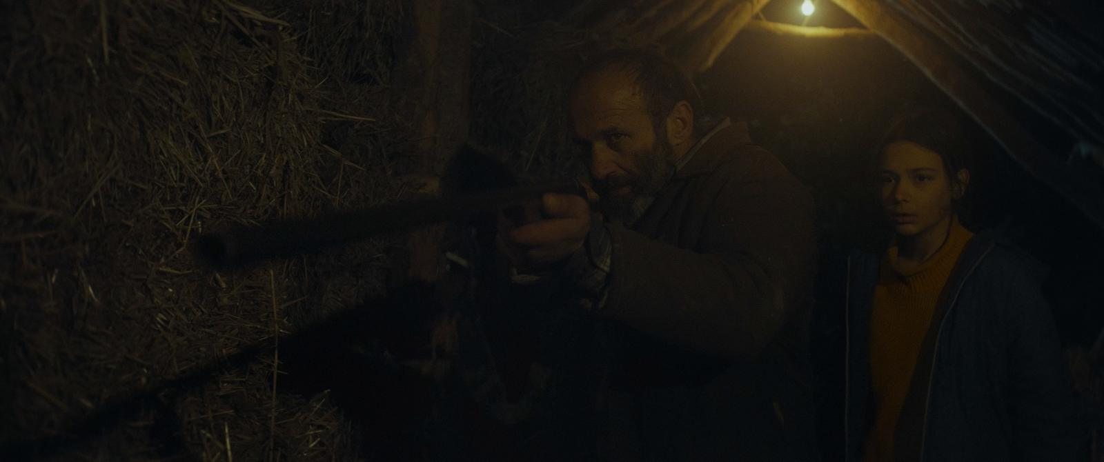 Damien aims a rifle in a hayloft while Luna watches. Still from OBITUS.